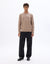Man wearing a beige sweater and black pants on a white background