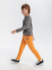 Child wearing a gray long-sleeve shirt and orange pants on a white background