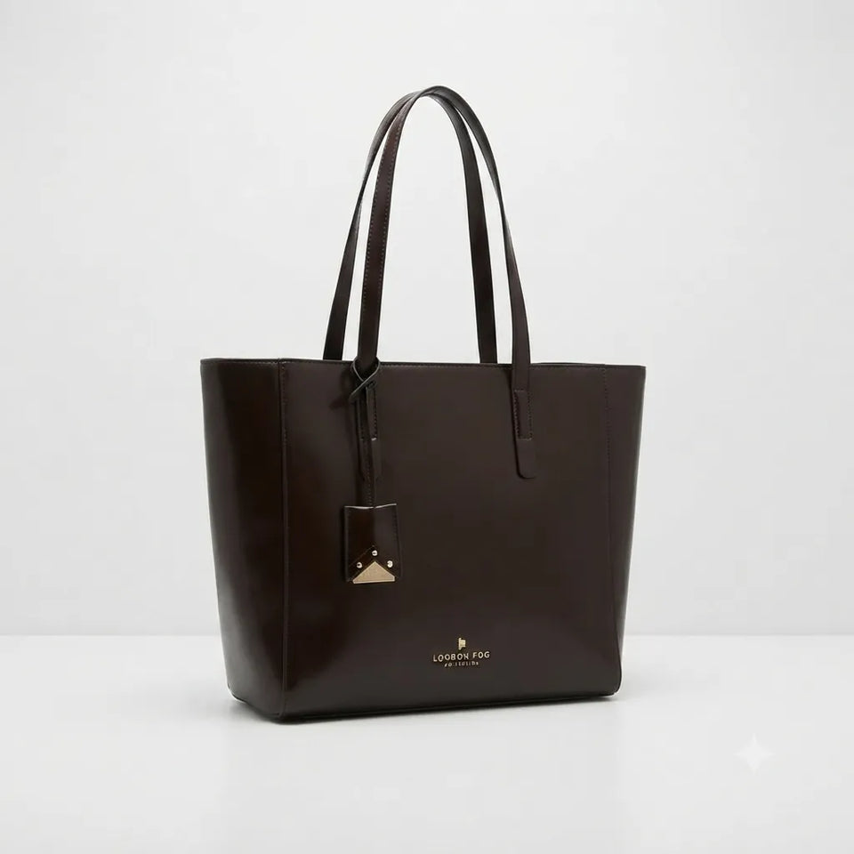 A dark brown leather tote bag with double shoulder straps, a hanging metal tag, and a small gold logo on the front, photographed against a clean white studio background.