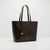 A dark brown leather tote bag with double shoulder straps, a hanging metal tag, and a small gold logo on the front, photographed against a clean white studio background.