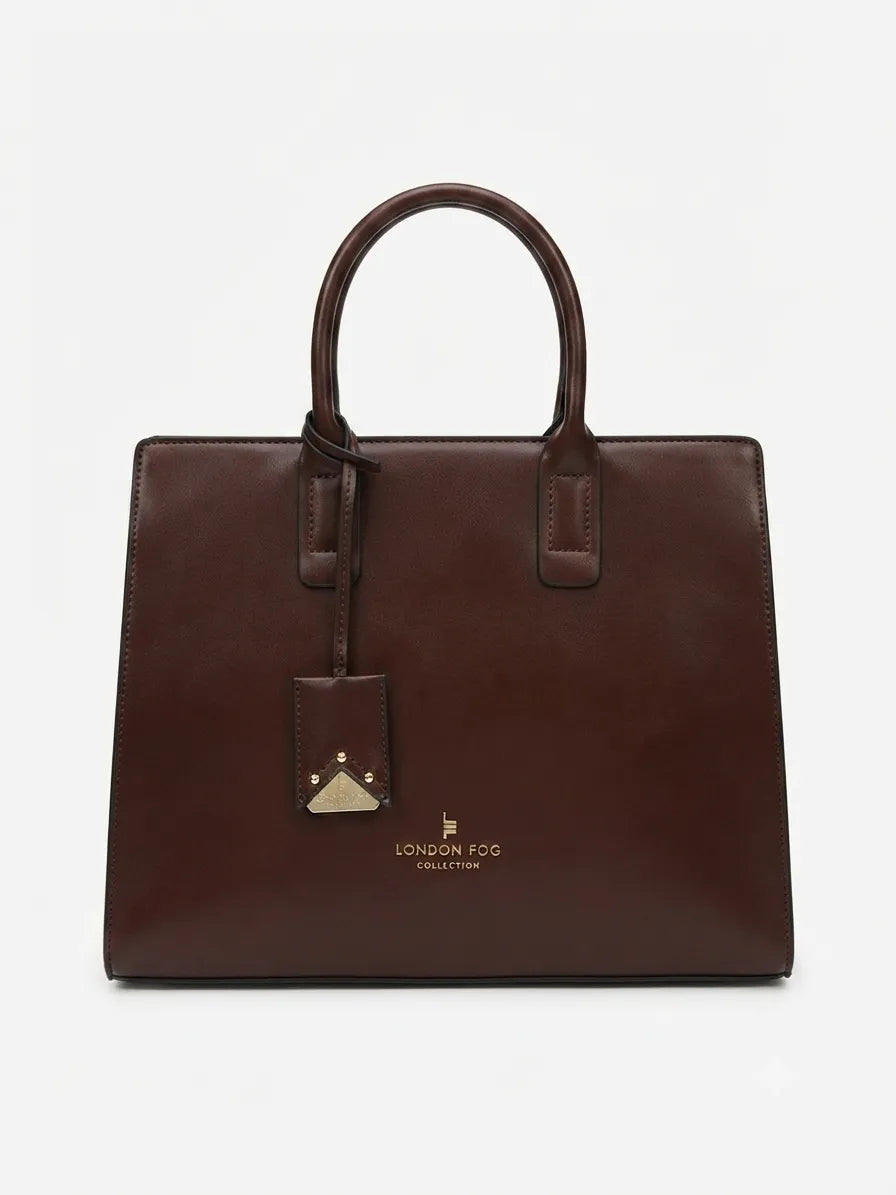 A dark brown leather tote bag with double top handles, a hanging leather tag, and gold-tone branding on the front, photographed against a clean white background.