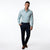 A man modeling a light blue long-sleeve button-down shirt with a small floral pattern, paired with dark navy trousers and brown leather shoes, against a plain white studio background.