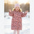 A young girl smiling in a snowy outdoor setting, wearing a pink floral puffer coat and a light pink beanie.