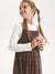 Young girl wearing a brown checkered pinafore dress over a white shirt on a white background