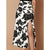 A high-waisted midi skirt with a black and white floral print and a thigh-high side slit, shown on a model against a solid tan background.