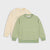 Two long-sleeve knit crewneck sweaters laid flat on a light gray background. The front sweater is light green and cream horizontally striped, while the back sweater is pale cream with a small green geometric line graphic on the left chest.