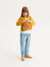 Child wearing a mustard yellow sweater and light blue jeans, holding a brown bag on a white background