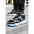 A pair of chunky low-top sneakers shown on a person standing on gray pavement. The shoes are primarily dark gray and black with light blue accents and a white midsole, paired with black socks.
