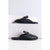 A pair of black leather slide sandals with a textured upper and a gold-tone buckle detail, displayed on white concrete steps against a light gray background.