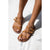 A pair of tan suede-like slide sandals with double straps and small metal buckles, shown on a model's feet against a bright white background.