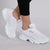 White chunky platform sneakers with a mesh upper and thick sculpted sole, shown on a model wearing black cropped leggings against a light gray studio background.