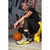 A man in athletic wear crouches on a concrete ledge in front of a graffiti-covered brick wall, with a basketball at his side. He is wearing a black t-shirt, black leggings, a gray and yellow running shoe, and a yellow jacket.