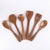 A set of six wooden kitchen utensils, including a salad spinner, spatula, spoons, and a fork, arranged in a fan shape on a plain white background.