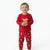 A toddler standing against a plain white studio background wearing a red long-sleeve pajama top with a Grinch graphic and matching red pajama pants with a green Grinch print.