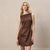 A blonde woman models a sleeveless brown mini dress with an asymmetrical neckline and a matching waist belt with a small silver buckle, set against a textured beige wall.