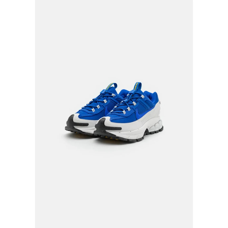 A pair of low-top sneakers in vibrant royal blue with a chunky white midsole, black toe caps, and small silver eyelet accents, set against a plain light gray background.