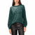 A woman wearing a dark green knit sweater covered in small white sequins, paired with black faux-leather pants, against a plain white background.