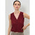 A woman modeling a sleeveless V-neck knit top in deep burgundy with a button-front closure, paired with patterned trousers, against a light gray studio background.