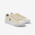 A pair of Lacoste low-top sneakers in a light cream canvas, featuring the signature green crocodile logo on the side and white rubber soles, set against a plain light gray background.