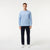 A man modeling a light blue long-sleeve crewneck sweater, paired with dark navy pants and white sneakers, against a plain white studio background.