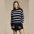 A woman modeling a navy blue and white horizontally striped knit sweater, paired with a black skirt, against a solid beige studio background.