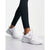 White Nike running shoes with a metallic silver Swoosh, shown on a model wearing black leggings against a light gray studio background.