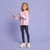 A young girl with curly blonde hair stands against a solid lavender studio background, wearing a light pink long-sleeve knit sweater, dark navy leggings with a small pink and white pattern, and off-white sneakers.