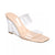 A clear wedge mule sandal with a nude beige footbed and transparent straps, shown from a three-quarters angle on a white background.