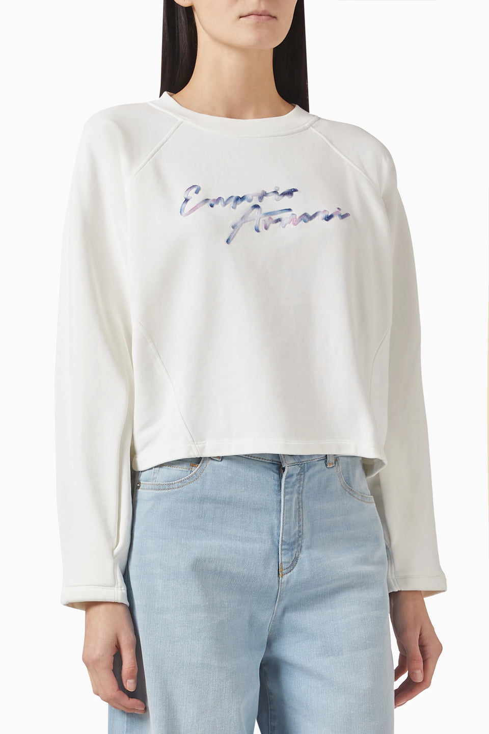 Person wearing a white sweatshirt with colorful text and light blue jeans on a white background