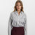 A woman modeling a long-sleeve button-up shirt with vertical black and white stripes, tucked into a dark burgundy mini skirt, against a plain white studio background.