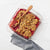 Glass dish with raspberry crumble dessert and wooden spoon on a white background