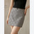 A model wearing a gray mini skirt with a subtle plaid pattern and a black top, shown from the chest down against a neutral beige background.