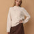 A woman wearing a cream-colored knit mock neck sweater and a brown skirt, posing against a solid tan background.