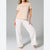 A woman modeling a two-piece pajama set consisting of a short-sleeve crewneck t-shirt in light beige and wide-leg pants in white with a subtle beige pattern, set against a plain gray studio background.