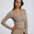 A woman modeling a beige long-sleeve ribbed knit top with a scoop neckline and a button-down front, paired with matching beige pants, against a light gray studio background.