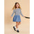 A young girl modeling a two-piece outfit consisting of a navy and white striped long-sleeve top with a small chest pocket, and a light blue denim skirt. She is wearing white socks and black Mary Jane shoes against a solid beige studio background.