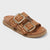 A single women's slide sandal with two woven brown straps featuring large square gold-tone buckles, set against a light gray background.