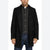 A man wearing a black mid-length overcoat over a black quilted button-front shirt and blue jeans, photographed against a plain white studio background.