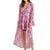 A woman modeling a long-sleeved pink floral midi dress with a tiered ruffle skirt and high-low hemline, paired with brown platform sandals against a plain white background.