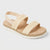 A single women's espadrille-style sandal in a light beige/tan color, featuring woven straps, a fabric ankle strap, and a white wavy sole, shown on a light gray background.