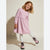 A young girl with blonde hair wearing a light pink long-sleeve dress with tiny dark polka dots, white tights, and pink lace-up boots, posing against a warm beige studio background.