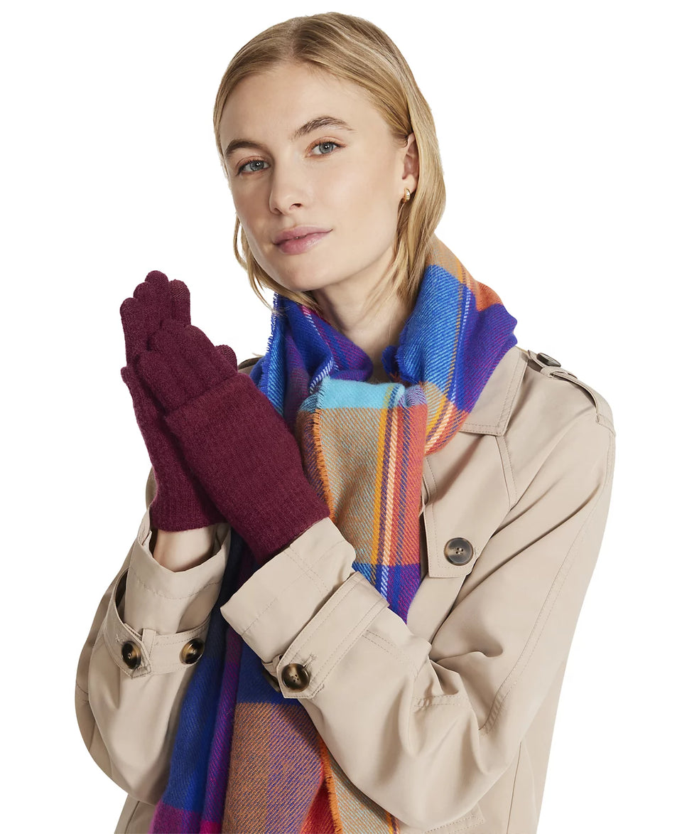 Woman wearing a beige trench coat, colorful scarf, and maroon gloves on a white background