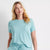 A woman modeling a matching light aqua two-piece loungewear set consisting of a short-sleeve crewneck top with a chest pocket and matching wide-leg drawstring pants, set against a plain white studio background.