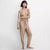 A woman modeling a ribbed knit two-piece loungewear set in a warm beige/tan color, consisting of a long-sleeve crewneck top and matching drawstring pants, against a plain light gray studio background.