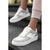 A pair of low-top platform sneakers in white and light gray with pale pink accents, shown on a model's feet standing on dark outdoor steps.