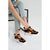 A person seated on a chair wearing black chunky platform sneakers with bright orange laces and orange side accents, paired with light blue frayed-hem jeans in a clean studio setting.