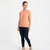 A woman modeling a sleeveless, high-neck ribbed knit top in a muted peach-pink color, paired with dark navy skinny jeans and beige heels, against a plain white studio background.