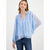 A woman wearing a light blue sheer long-sleeve blouse with a smocked V-neck bodice and drawstring details, paired with dark blue jeans, against a plain white studio background.