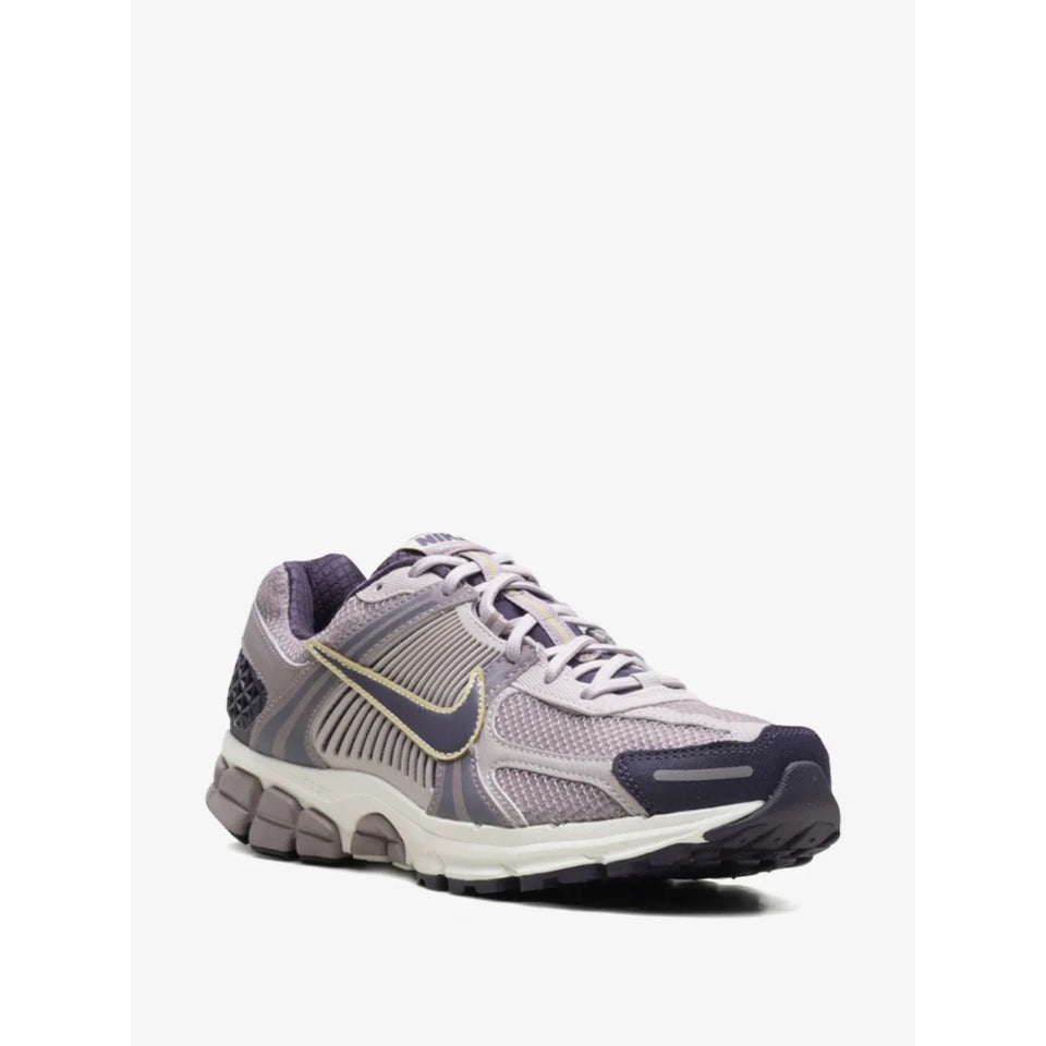 A Nike running shoe in a mix of lavender, gray, and navy blue, featuring a gold Swoosh accent, set against a plain light gray background.