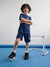 Child wearing a blue sports outfit with number 3, standing on a blue floor with a small soccer goal in the background.
